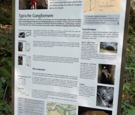 Informational sign about the Ibachhöhle cave with photos, diagrams, a map, and cartoons.